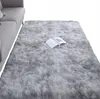 A soft, shaggy rug in a light gray color is shown in a living room setting next to a sofa. An open book rests on the rug. Podgląd zdjęcia produktu