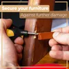 A close-up shot of hands repairing a wooden furniture leg with a repair tool and a piece of brown wax. Voir les images du produit