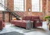 A modern living room with exposed brick walls and a loft-style staircase, featuring a dusty rose sectional sofa with a grey throw blanket. Produktbild-Vorschau