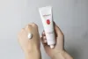 A hand is holding a tube of cream, with a dollop of cream on another hand. Náhled obrázku produktu