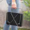 A person is holding a portable charcoal grill outdoors. Náhled obrázku produktu