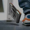 A person's leg and foot are visible next to a smartphone case that is falling. Náhled obrázku produktu
