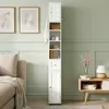 A tall, narrow white cabinet with shelves and a drawer stands next to a sofa and a side table in a room with green walls. Produktbild-Vorschau