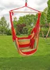 A striped hammock chair is hanging in a grassy backyard with trees and a swing set in the background. Náhled obrázku produktu