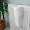 A white radiator humidifier is attached to a white radiator. A potted plant is visible in the background. Náhľad obrázku produktu