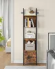A tall, narrow bookshelf with a rustic wood finish and black metal frame, filled with books and decorative items. It is placed in a room with a bed and curtains visible in the background, and a sofa on the right. Produktbild-Vorschau