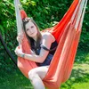 A young woman is relaxing in an orange hammock chair outdoors. Podgląd zdjęcia produktu