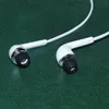 A pair of white earbuds with black tips and silver accents rests on a dark green textured surface. Náhľad obrázku produktu