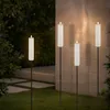 Four solar-powered candle-shaped lights are placed in a garden at dusk, illuminating a stone wall and surrounding greenery. Anteprima dell’immagine prodotto