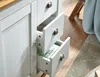 A close-up view of a white sideboard with three drawers, one of which is partially open, revealing a green and white polka dot lining. The image also shows a wooden countertop and a portion of a wooden floor. Náhľad obrázku produktu