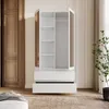 A white wardrobe with open doors and drawers, placed in a room with wooden doors and a plant. Produktbild-Vorschau