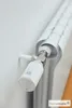 A close-up shot of a smart home radiator thermostat attached to a radiator, with a white wall in the background. Produktbild-Vorschau