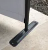A close-up view of the base of a grey fabric screen, showing its black metal support pole and a flat metal base plate attached to the ground. Produktbild-Vorschau
