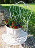 A white metal chair with a pot of red and purple flowers on it, placed outdoors in a garden setting. Voir les images du produit