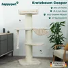 A cream-colored cat tree is shown in a room with a plant and a chair. Podgląd zdjęcia produktu