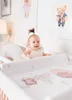 A baby sitting in a crib with a changing pad. Produktbild-Vorschau
