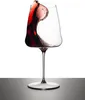 A wine glass with red wine splashing inside, set against a white background and on a dark surface. Produktbild-Vorschau
