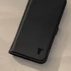 A black leather phone case with a bull logo embossed on it, lying on a light gray textured surface. Produktbild-Vorschau
