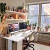 A home office setup with a desk, computers, shelves, and plants, with a city view from the window. Anteprima dell’immagine prodotto
