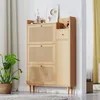 A wooden shoe cabinet with rattan doors and a drawer, placed against a wall with curtains and a plant. Podgląd zdjęcia produktu