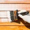 A hand wearing a white glove is painting a wooden surface with a brush dipped in white paint. Produktbild-Vorschau
