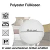 A round polyester cushion is shown on a bed with other cushions. Produktbild-Vorschau