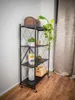 A black metal shelving unit with various decorative items and plants on its shelves, placed next to a wall and curtains. Produktbild-Vorschau