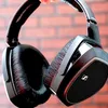 A close-up shot of a pair of black headphones against a brick wall background. Produktbild-Vorschau