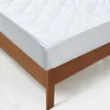 A white quilted mattress protector is shown on a wooden bed frame. Náhled obrázku produktu