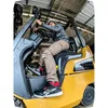 A person wearing work boots is sitting in a forklift. Náhľad obrázku produktu