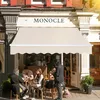 People sitting at tables outside a cafe under a beige awning. Podgląd zdjęcia produktu