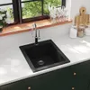 A black granite sink with a silver faucet is shown on a white countertop, with a window and kitchen items in the background. Voir les images du produit