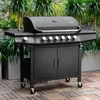 A black gas grill with a red logo sits on a wooden deck, surrounded by lush green plants. Produktbild-Vorschau