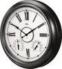 A close-up, angled view of a large, round wall clock with Roman numerals and two smaller dials for temperature and humidity. Produktbild-Vorschau