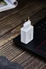 A white USB charger sits on a black laptop keyboard, with a magazine in the background on a wooden desk. Náhled obrázku produktu