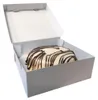 A white cake box with the lid open, containing a single cake decorated with white icing and dark chocolate drizzle. Produktbild-Vorschau