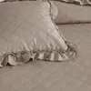 A close-up view of a quilted bedspread and pillow with ruffled edges. Produktbild-Vorschau