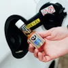 A hand is holding a small bottle of diesel fuel additive next to a car's fuel filler neck. Produktbild-Vorschau