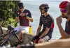 Cyclists taking a break by the water, eating energy gels. Produktbild-Vorschau