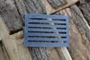 A dark gray metal grate with horizontal slots lies on a pile of chopped wood. Náhled obrázku produktu