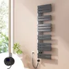 A modern anthracite electric towel radiator mounted on a light pink wall next to a window with greenery visible outside. A close-up inset shows the digital controller with a temperature display. Voir les images du produit