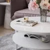 A modern living room scene with a round coffee table featuring books, a decorative cup, and flowers. Produktbild-Vorschau