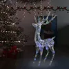 A lit-up acrylic reindeer decoration stands in a room with a Christmas tree and presents. Náhľad obrázku produktu