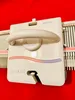 A knitting machine is shown against a red background. Produktbild-Vorschau