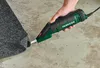 A hand holding a PARKSIDE electric scraper, using it to cut a piece of carpet. Produktbild-Vorschau