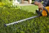A person is using a hedge trimmer to trim a green hedge in a garden setting. Produktbild-Vorschau
