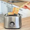 A hand is using wooden tongs to remove two slices of toasted bread from a silver toaster in a kitchen setting. Náhled obrázku produktu