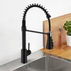 A black kitchen faucet with a coiled hose is shown in a kitchen sink area. Podgląd zdjęcia produktu