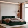 A bedroom with a large upholstered bed in dark green velvet. The bed has a tufted headboard and is made up with pillows and a throw blanket. A bedside table and a floor lamp are visible. A large window with curtains is in the background. Anteprima dell’immagine prodotto
