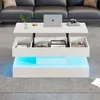 A modern white lift-top coffee table with hidden storage and blue LED lighting is placed on a gray rug in a living room. A laptop, a cup, a camera, and books are on the table. Produktbild-Vorschau